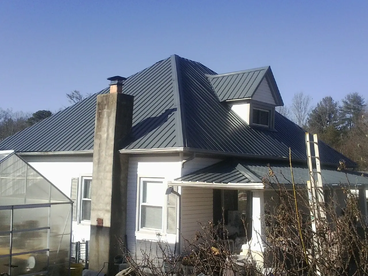Dark blue standing seam metal roof on a white farmhouse with dormer in Ogden