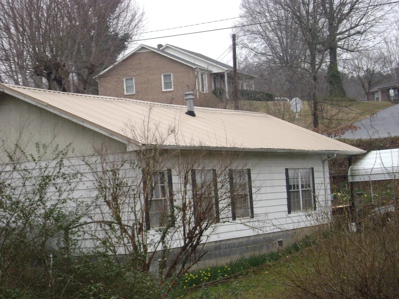 Tan metal roof on a white sided house set into a hillside — Commercial Roofing by Roofing Brothers in Ogden