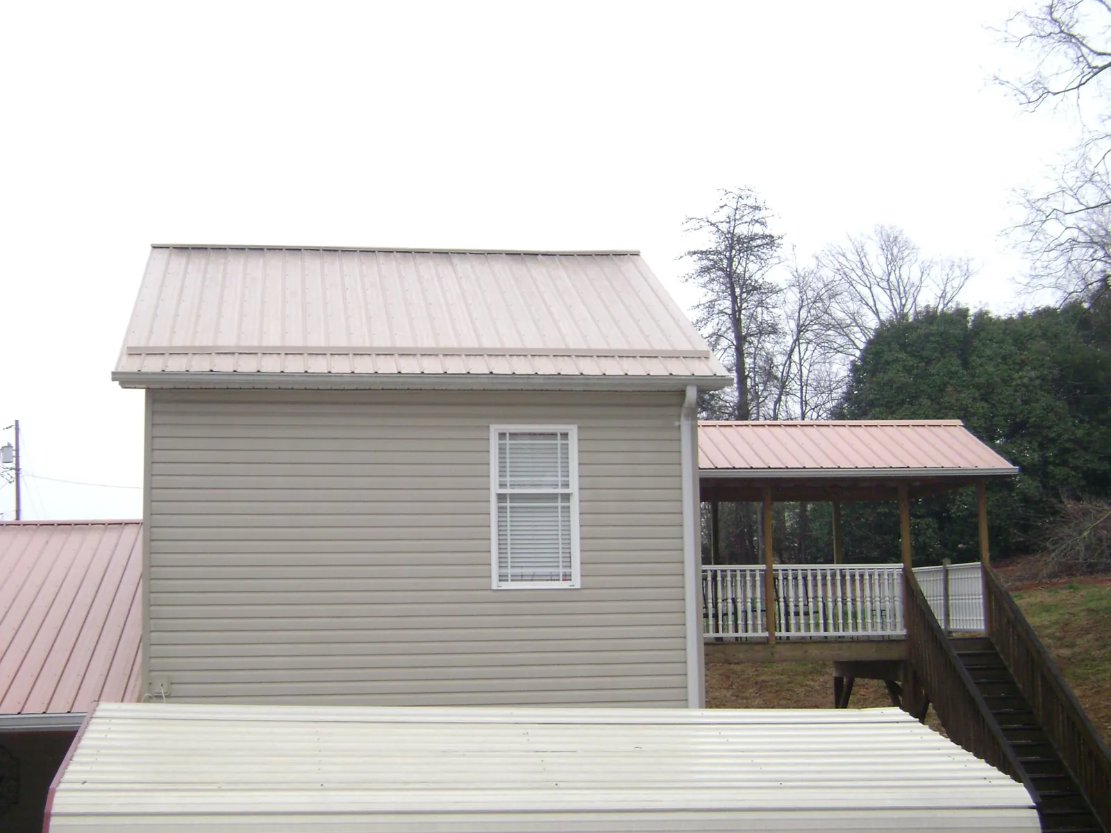 Tan metal roofs on a two story addition and attached porch, from a Roof Replacement job in Ogden
